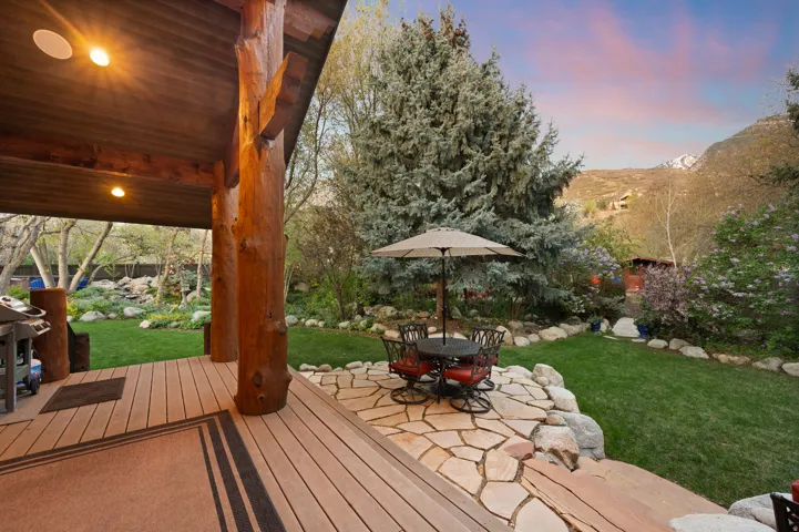 Deck at dusk with a yard, outdoor dining space, a patio area, a mountain view, and a grill