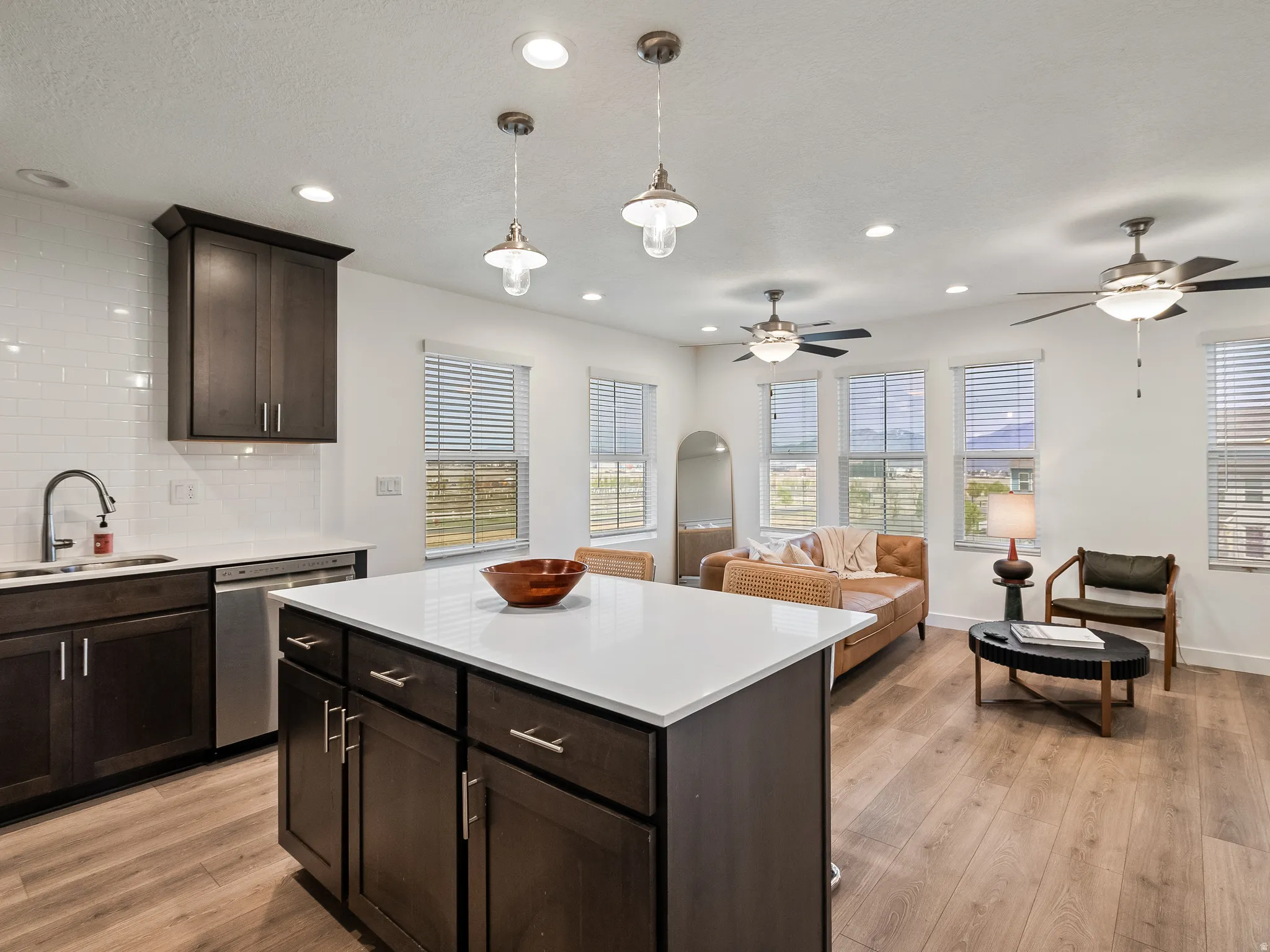 Kitchen featuring dark wood finish cabinetry, light wood-style flooring, decorative backsplash, stainless steel dishwasher, and a center island