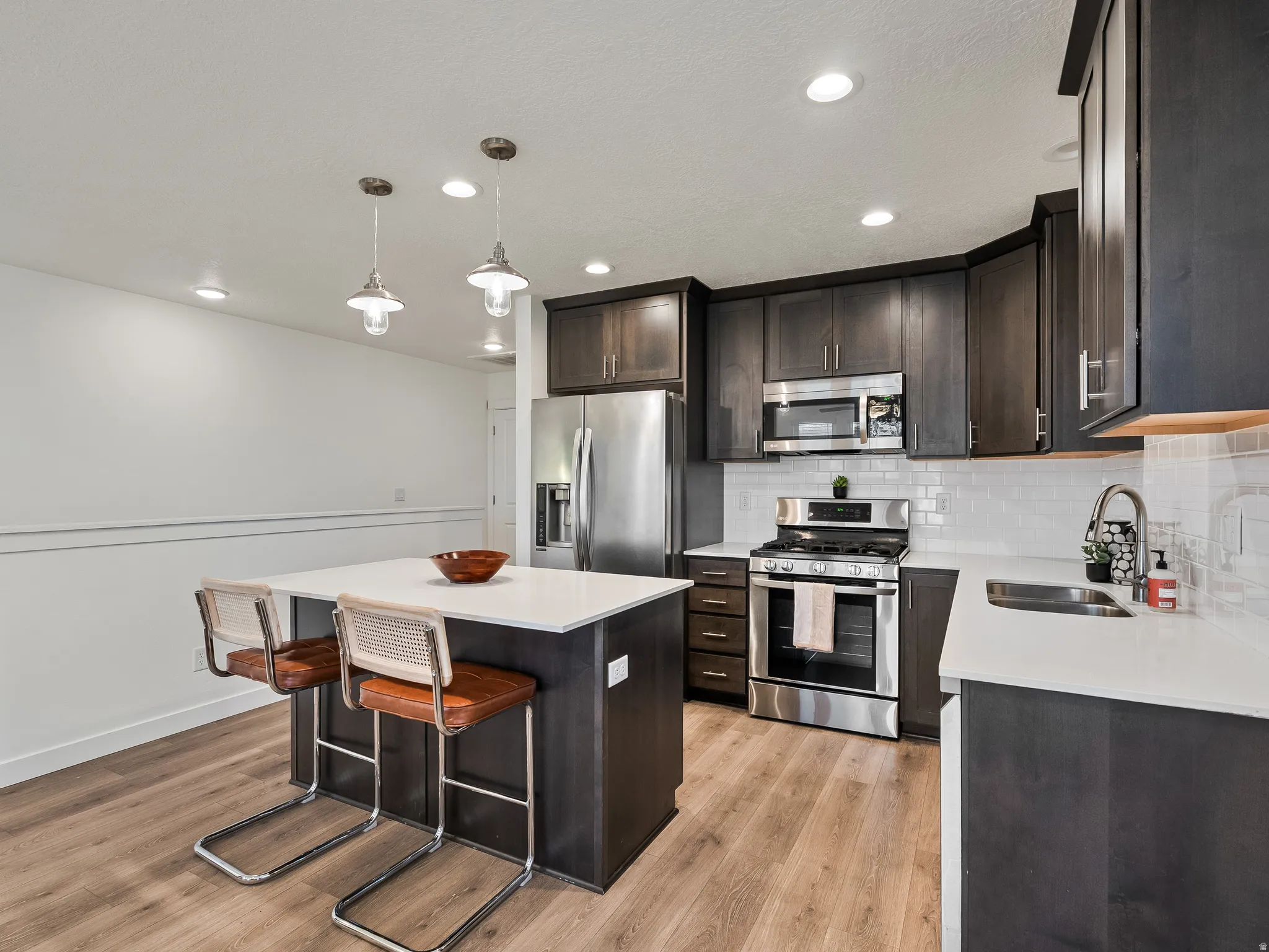 Kitchen featuring stainless steel appliances, dark wood finish cabinetry, light wood-style floors, a kitchen island, and hanging light fixtures