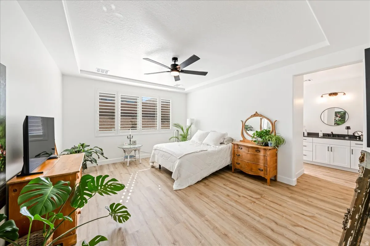 Bedroom featuring a raised ceiling, light wood-type flooring, a textured ceiling, and ceiling fan