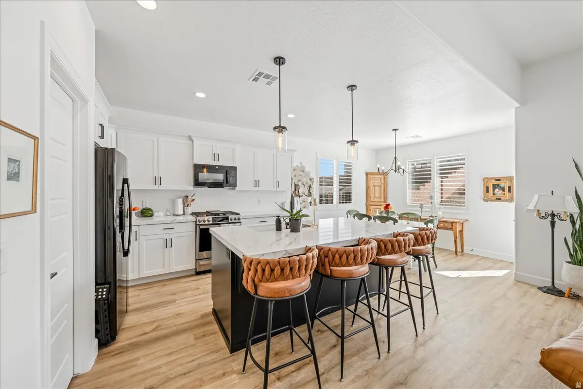 Kitchen with black appliances, a breakfast bar area, light wood-style floors, an island with sink, and light stone countertops
