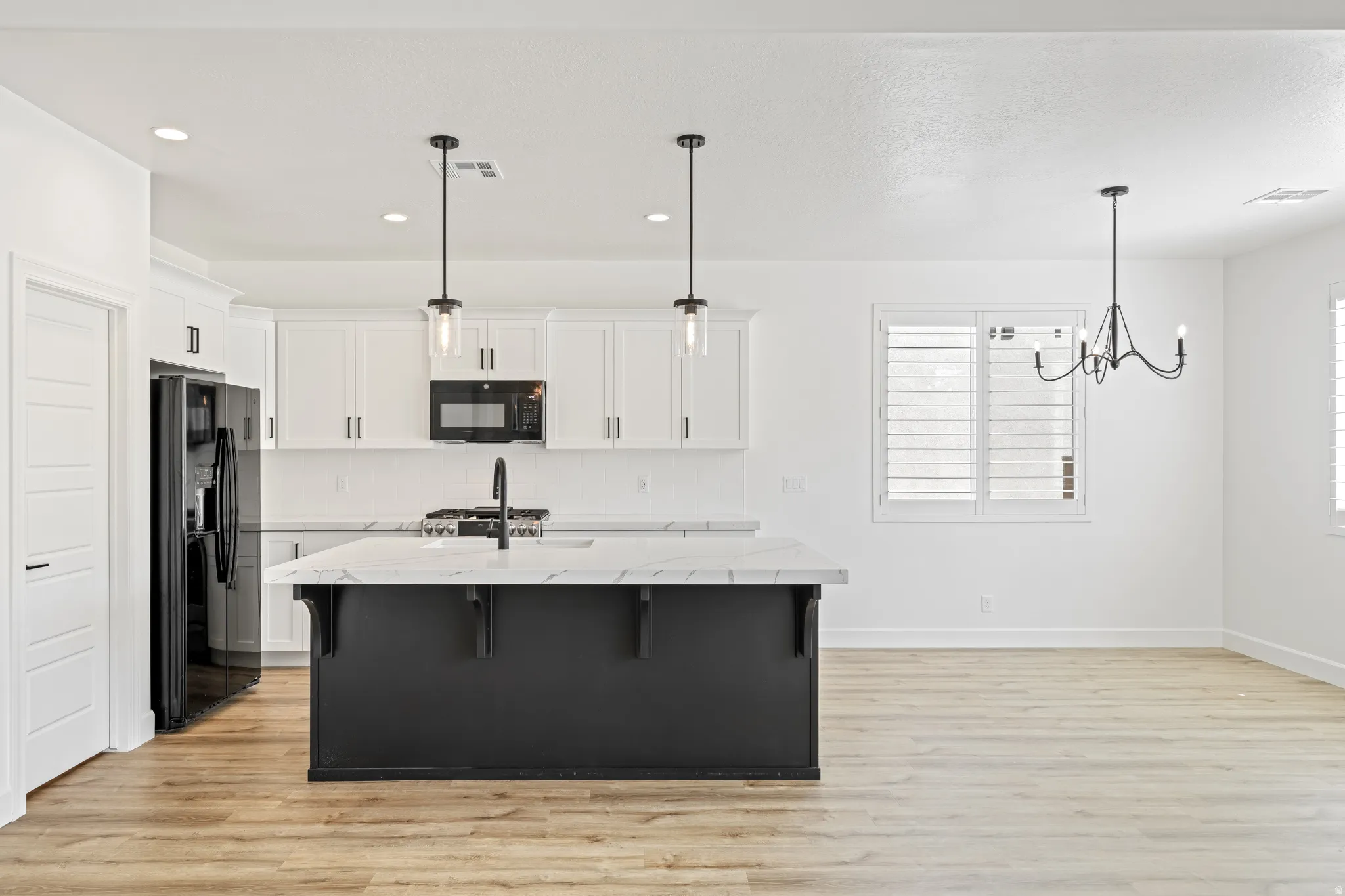 Dual tone kitchen with a breakfast bar area, a center island with sink, light wood-type flooring, black appliances, and two tone color scheme