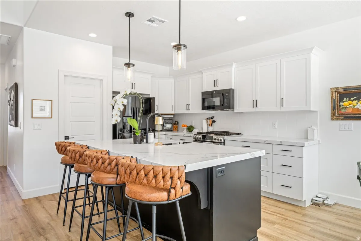 Kitchen with a kitchen island with sink, a kitchen bar, stainless steel appliances, light wood-style floors, and light stone countertops