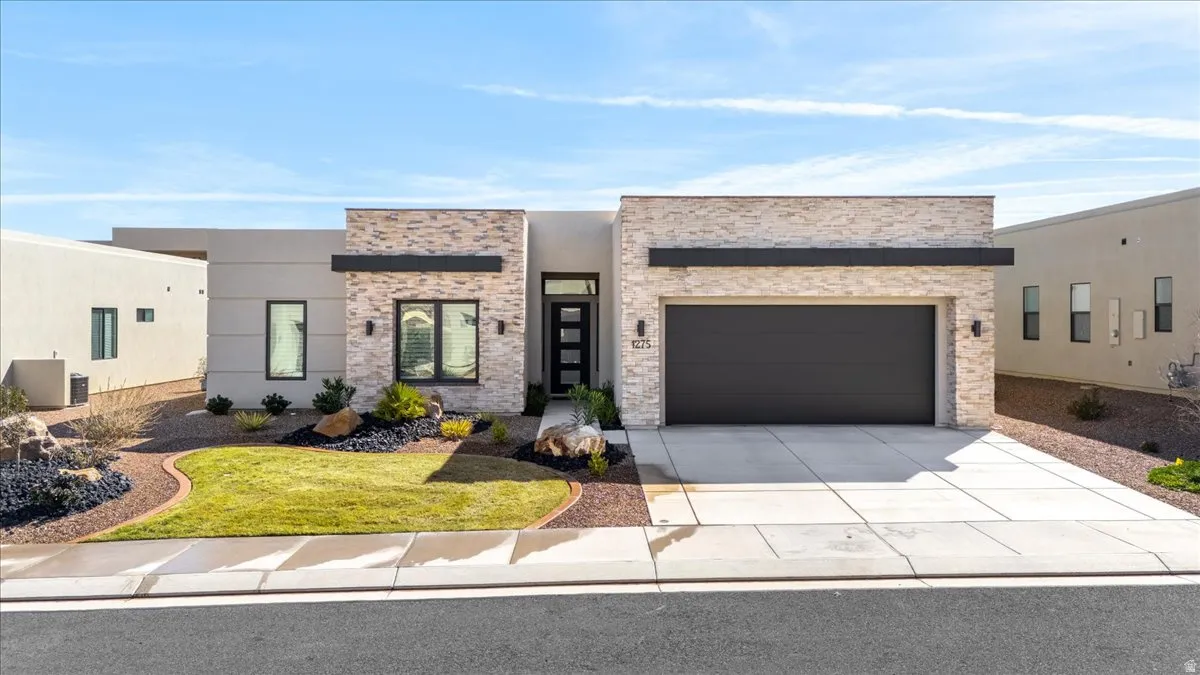 Modern home featuring a garage, concrete driveway, a front lawn, and stucco siding
