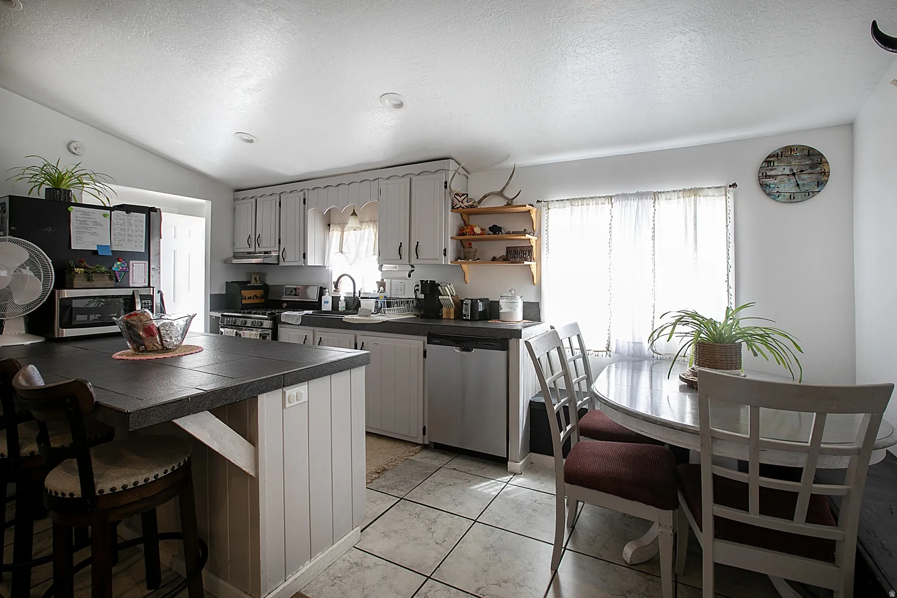Kitchen featuring stainless steel appliances, a kitchen bar, gray cabinetry, and open shelves