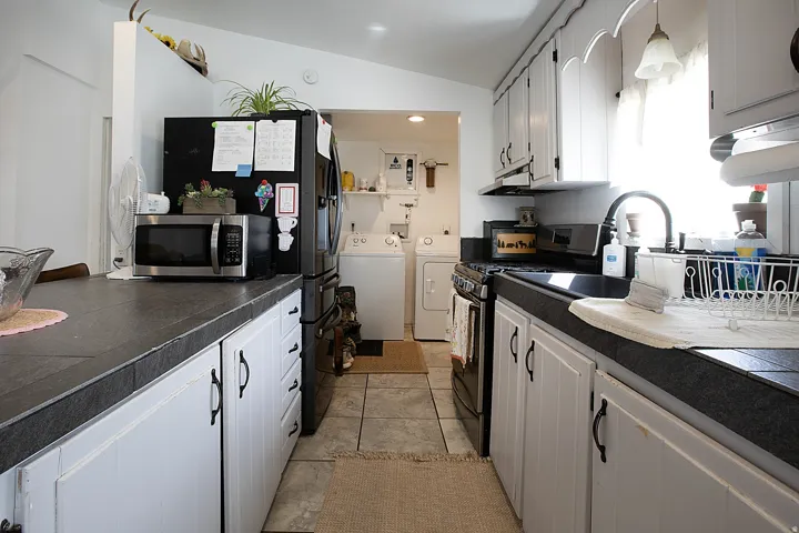 Kitchen featuring stainless steel appliances, white cabinetry, vaulted ceiling, washing machine and clothes dryer, and light tile patterned floors
