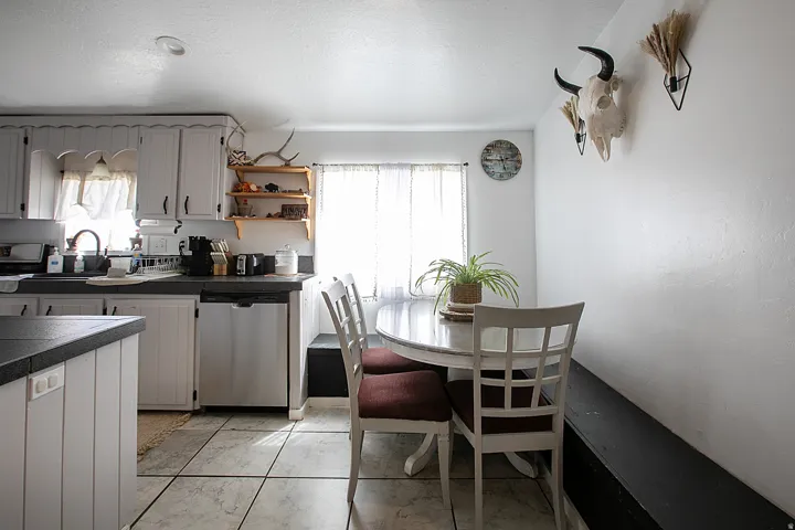 Kitchen with stainless steel dishwasher, open shelves, white cabinetry, tile countertops, and light marble finish floors