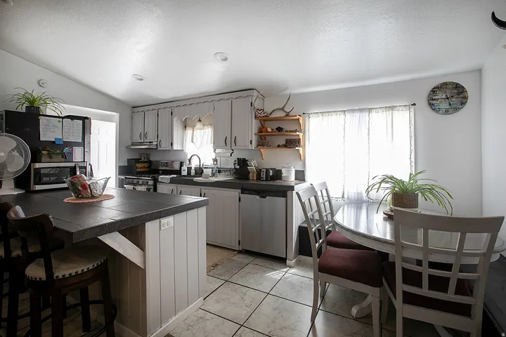 Kitchen featuring stainless steel appliances, a kitchen bar, gray cabinetry, and open shelves