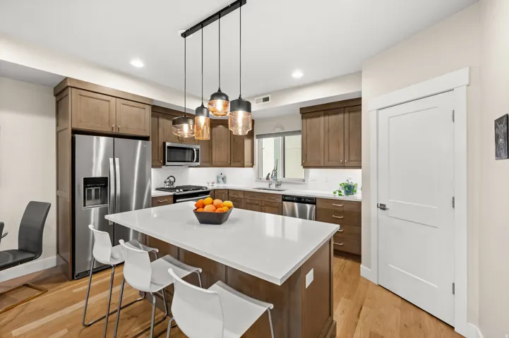 Kitchen with stainless steel appliances, light wood-style floors, a kitchen bar, a kitchen island, and light stone countertops
