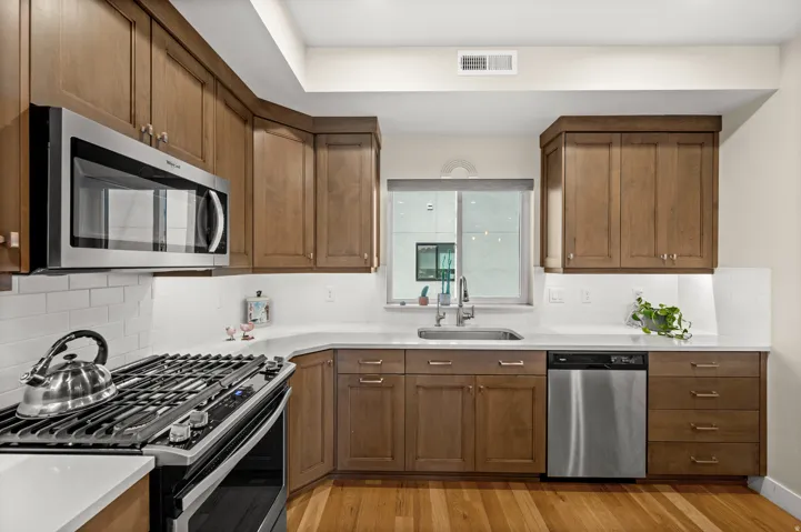 Kitchen featuring stainless steel appliances, tasteful backsplash, wood finish cabinets, and light wood finished floors
