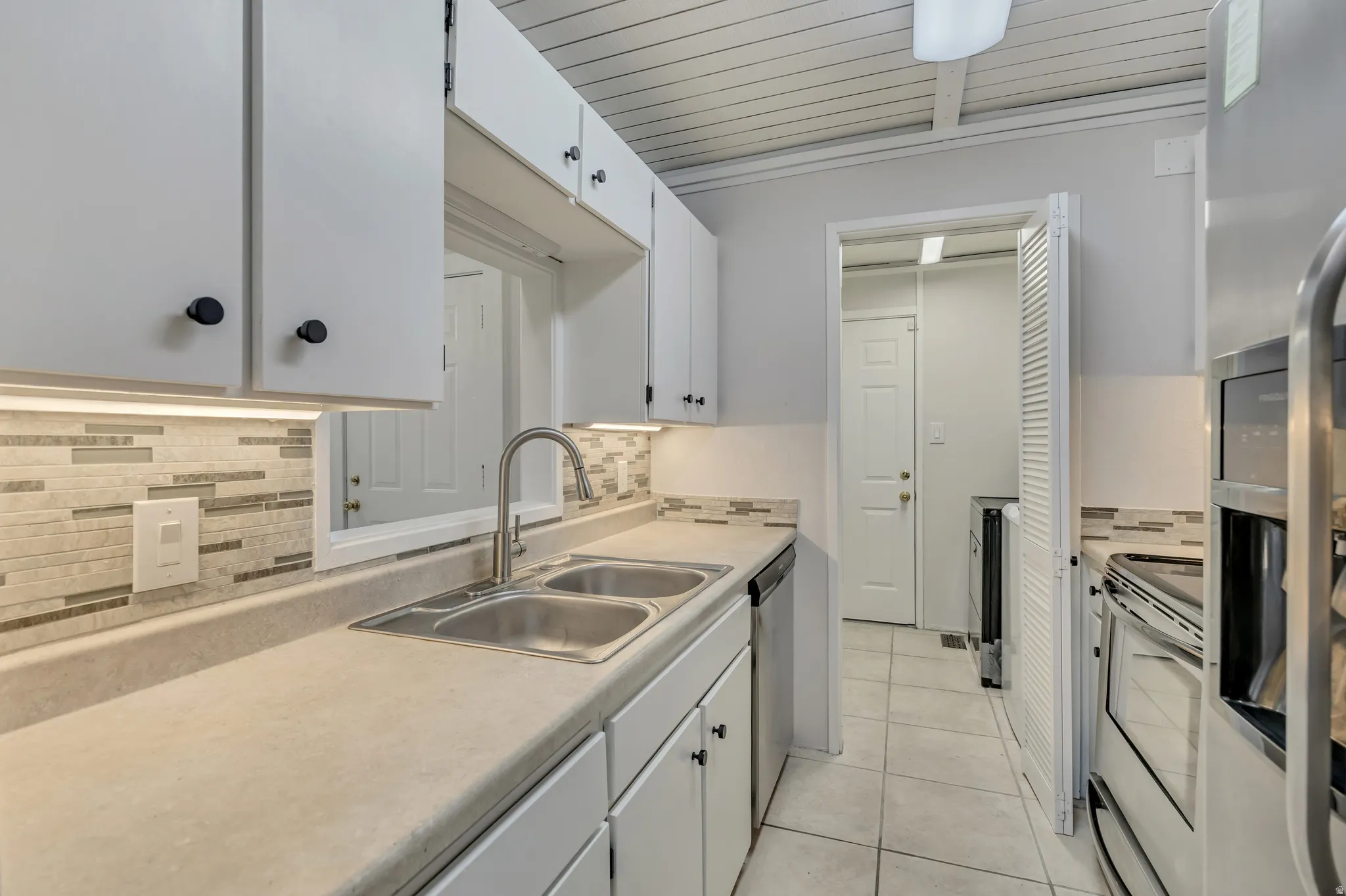 Kitchen featuring white cabinetry, stainless steel appliances, light countertops, light tile patterned floors, and tasteful backsplash