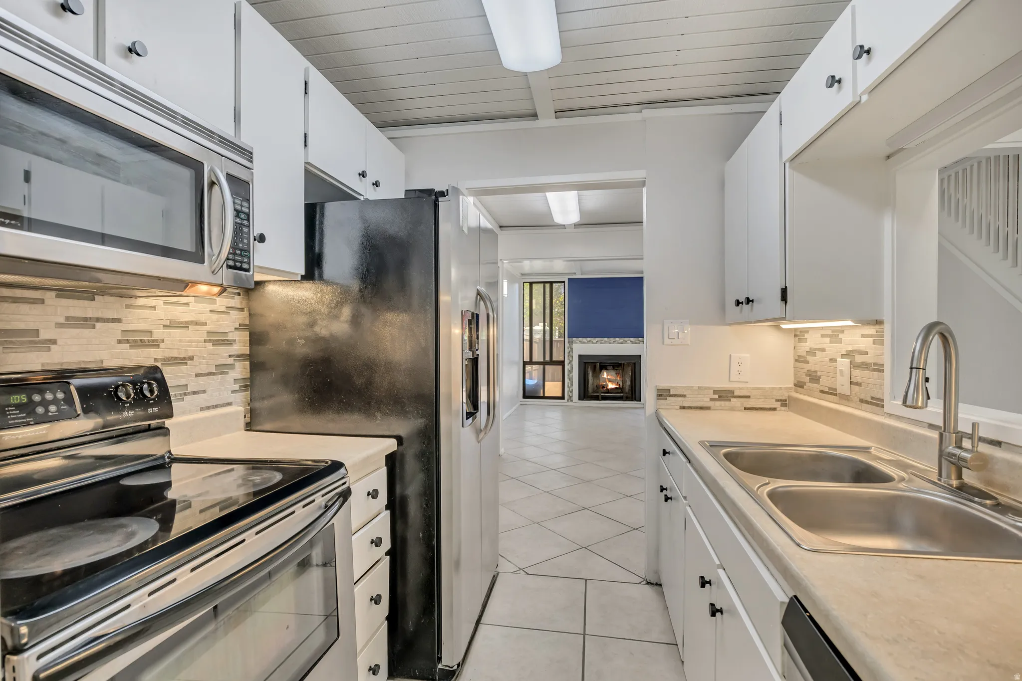 Kitchen with stainless steel appliances, light countertops, a warm lit fireplace, backsplash, and wooden ceiling