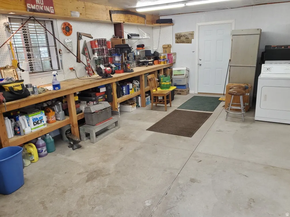 Utility space featuring concrete flooring, a white paneled door, a built-in workbench with shelving, and a window with horizontal blinds