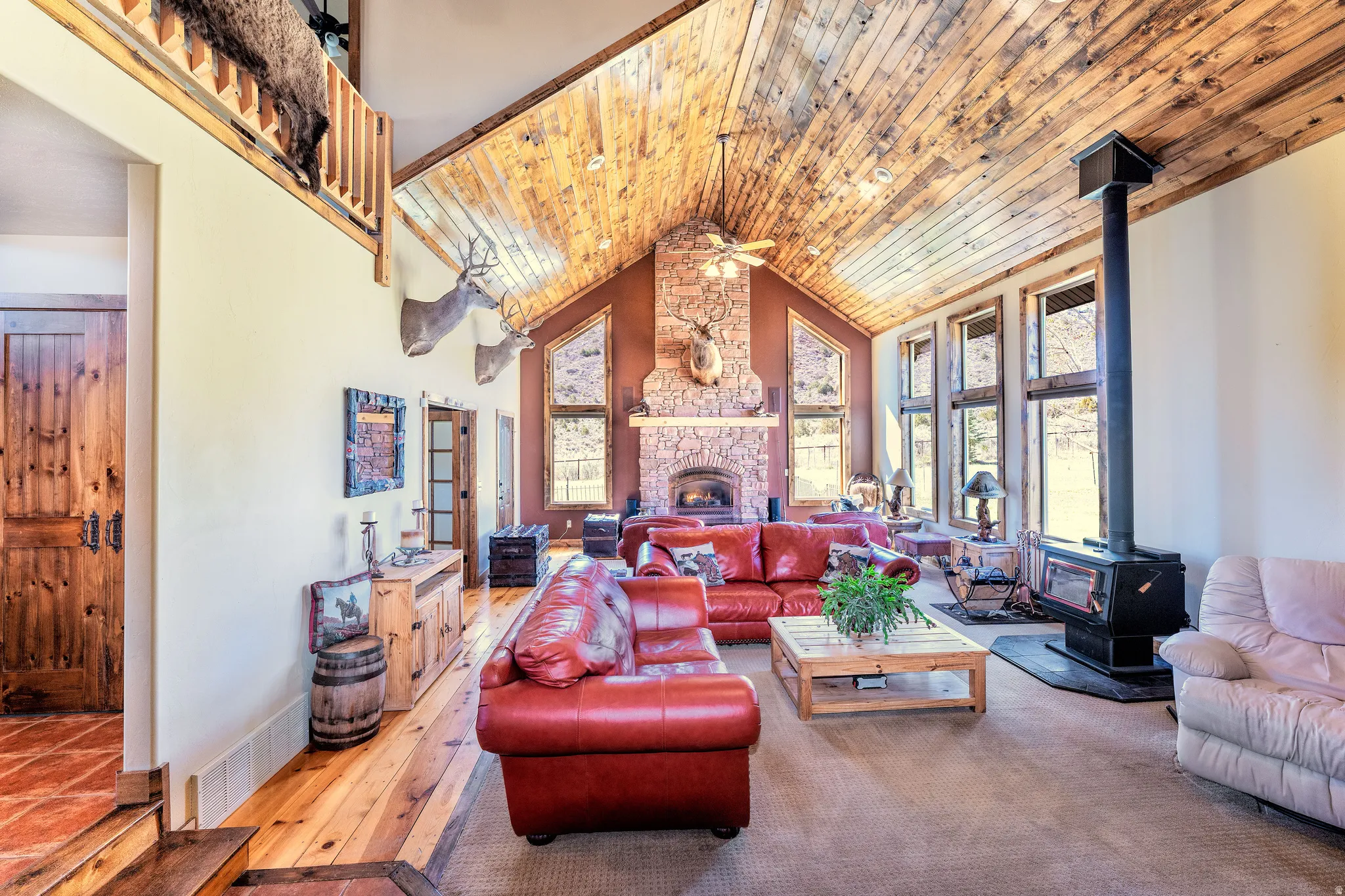 Living room with tongue & groove 24' vaulted ceiling, wood & carpet flooring, ceiling fan, a gas fireplace and a Blaze King wood catalytic stove.