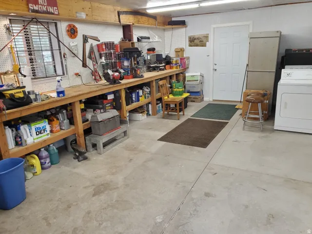 Utility space featuring concrete flooring, a white paneled door, a built-in workbench with shelving, and a window with horizontal blinds