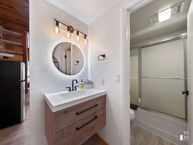 Full bath with a textured wall, vanity, shower / bath combination with glass door, and light wood-style floors
