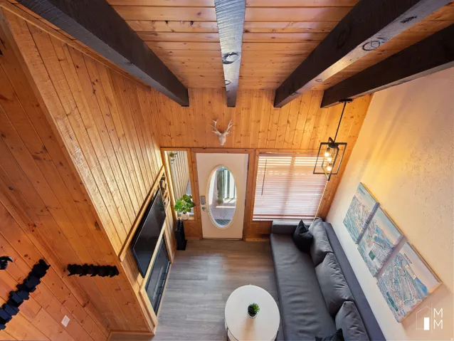Living room with wooden walls, dark wood-style flooring, and a wooden ceiling with exposed beams