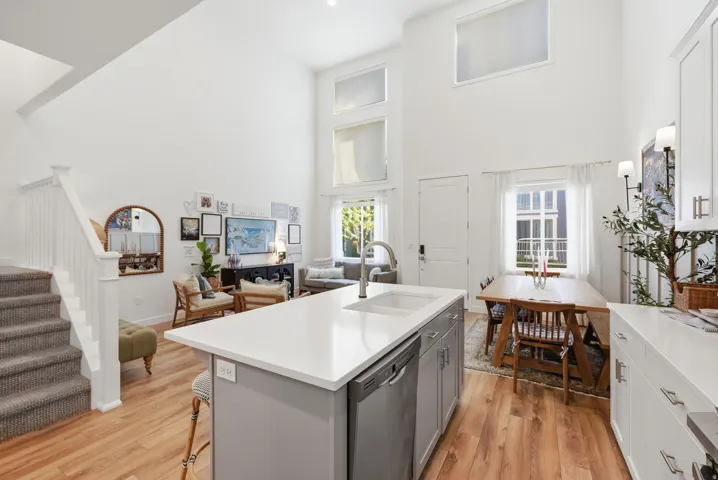 Kitchen featuring open floor plan, stainless steel dishwasher, a high ceiling, a kitchen bar, and an island with sink