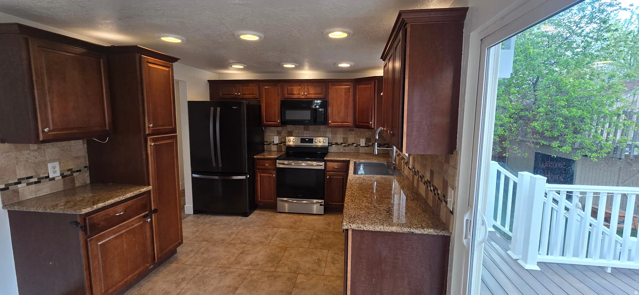 Kitchen with black appliances, tasteful backsplash, dark stone countertops, recessed lighting, and a textured ceiling