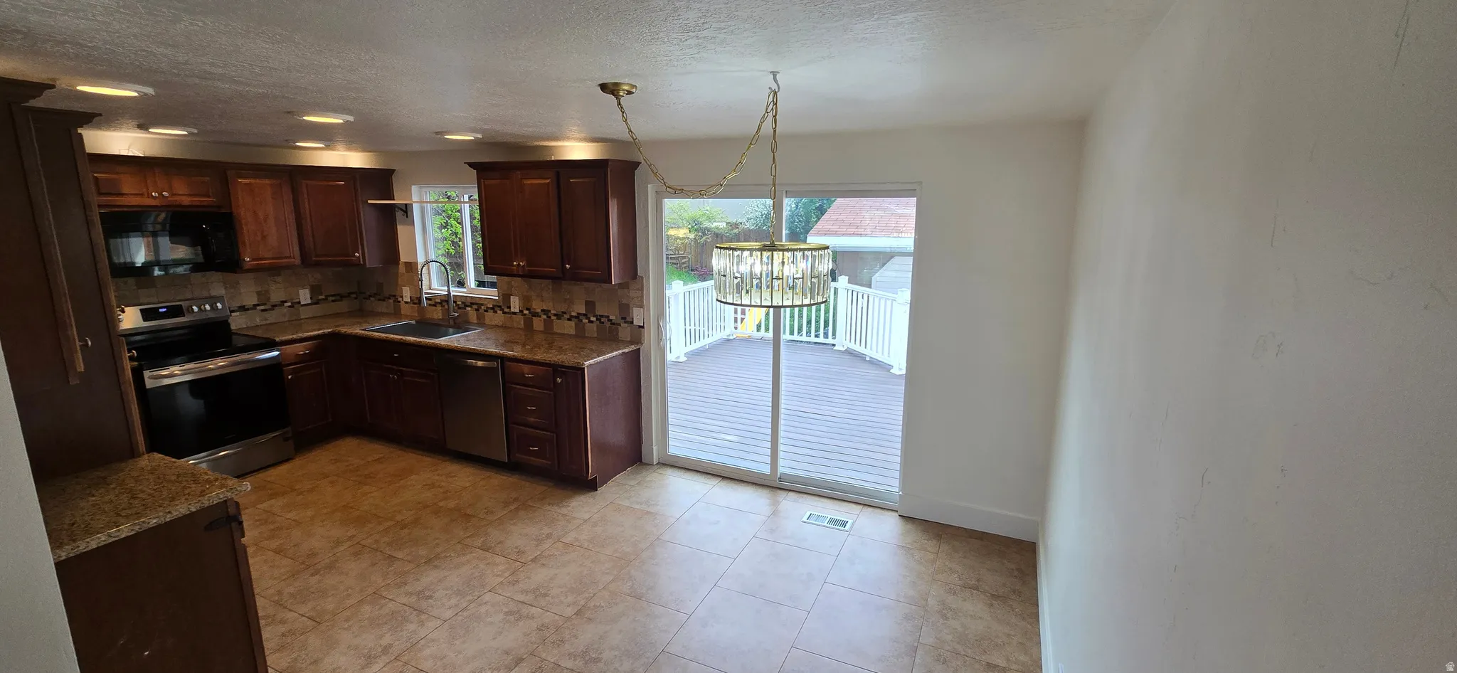 Kitchen featuring stainless steel appliances, dark wood finish cabinets, tasteful backsplash, dark stone countertops, and a textured ceiling