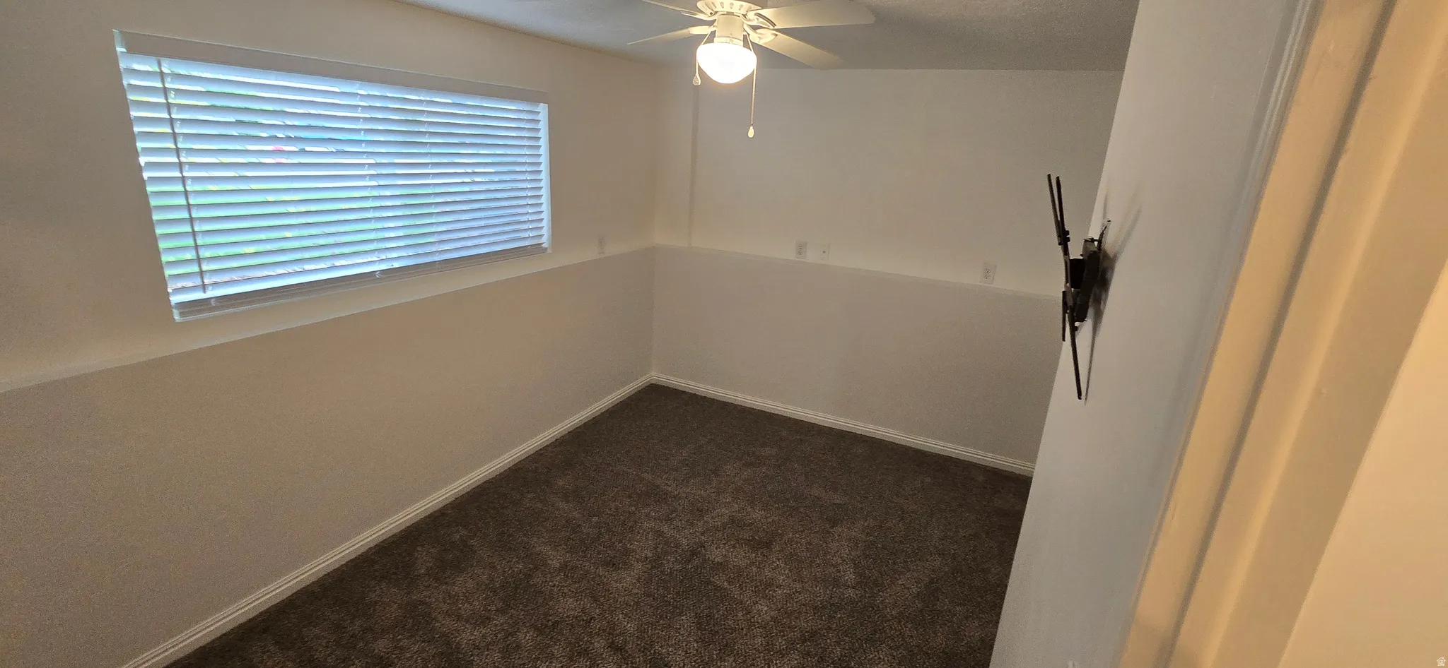 Empty room featuring dark colored carpet and a ceiling fan