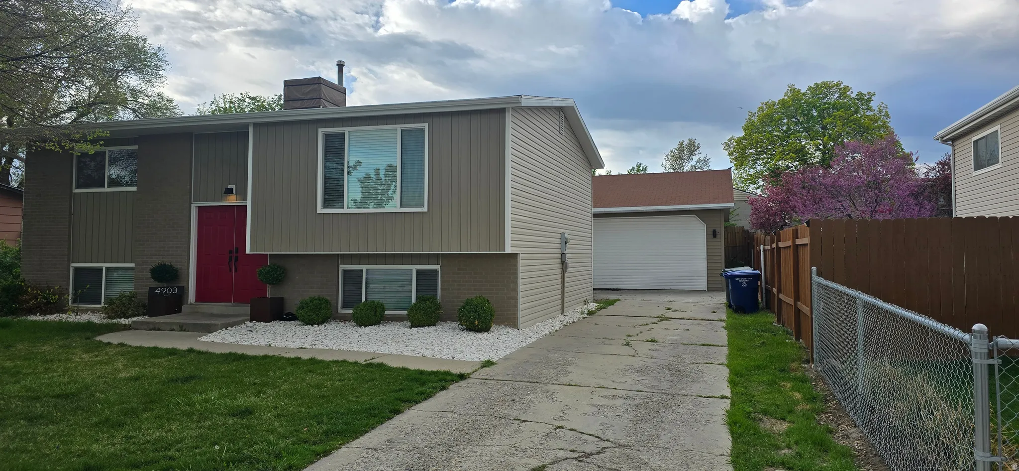 Raised ranch featuring brick siding, an outbuilding, a chimney, concrete driveway, and a detached garage