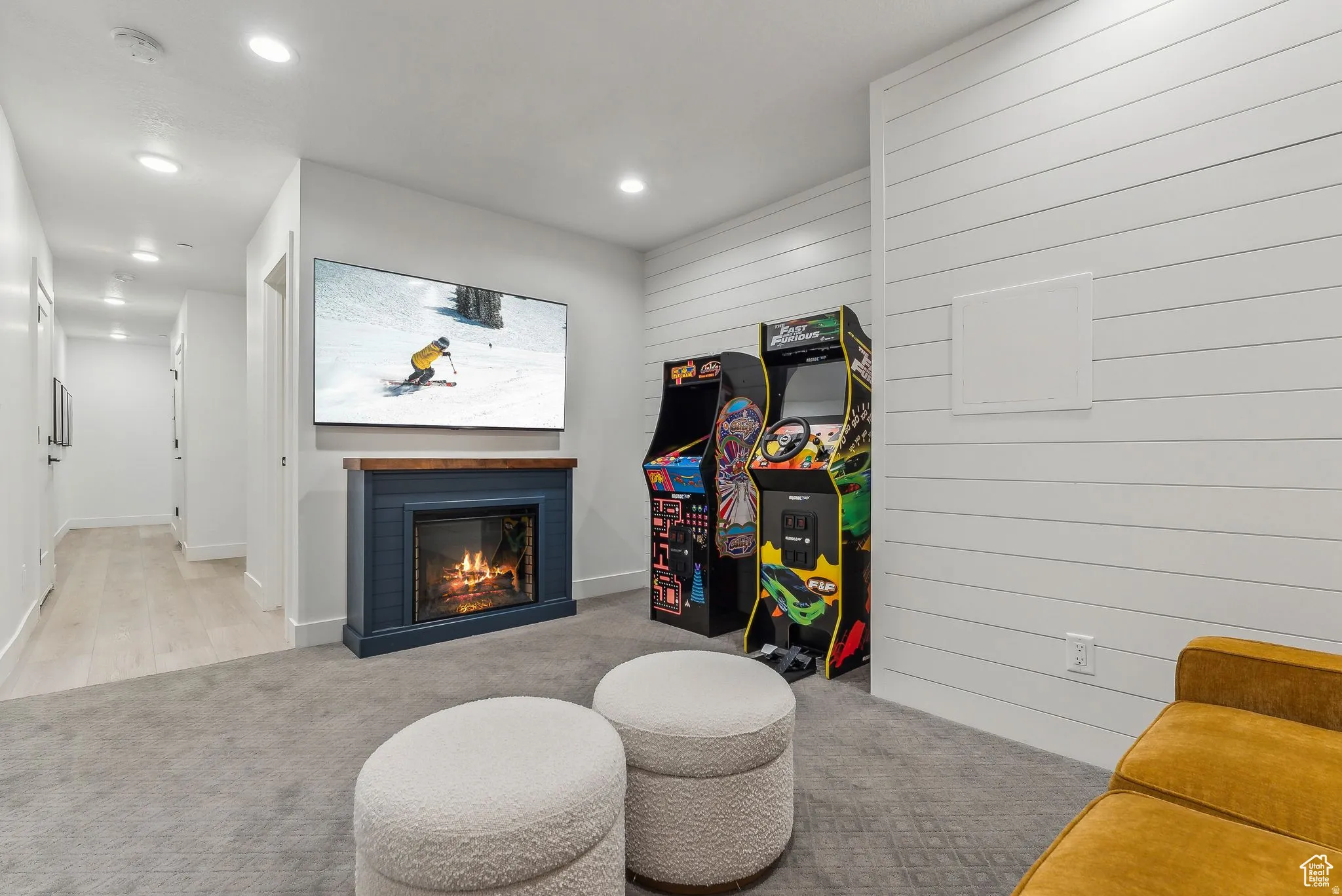 Rec room with a warm lit fireplace, light carpet, wooden walls, and recessed lighting