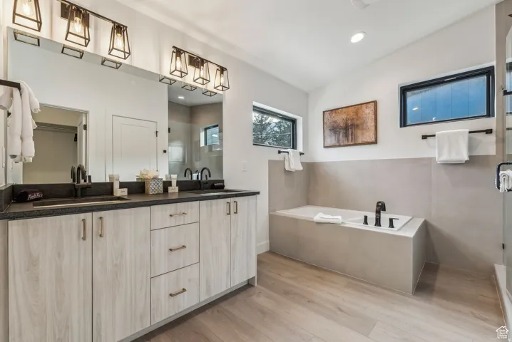 Full bathroom with double vanity, a garden tub, a shower stall, light wood-style floors, and recessed lighting
