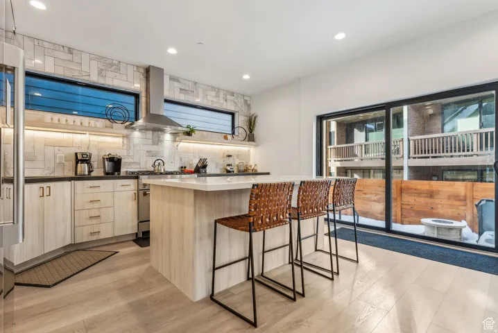 Kitchen with light wood finish cabinetry, a kitchen island, light wood-style floors, a kitchen bar, and backsplash