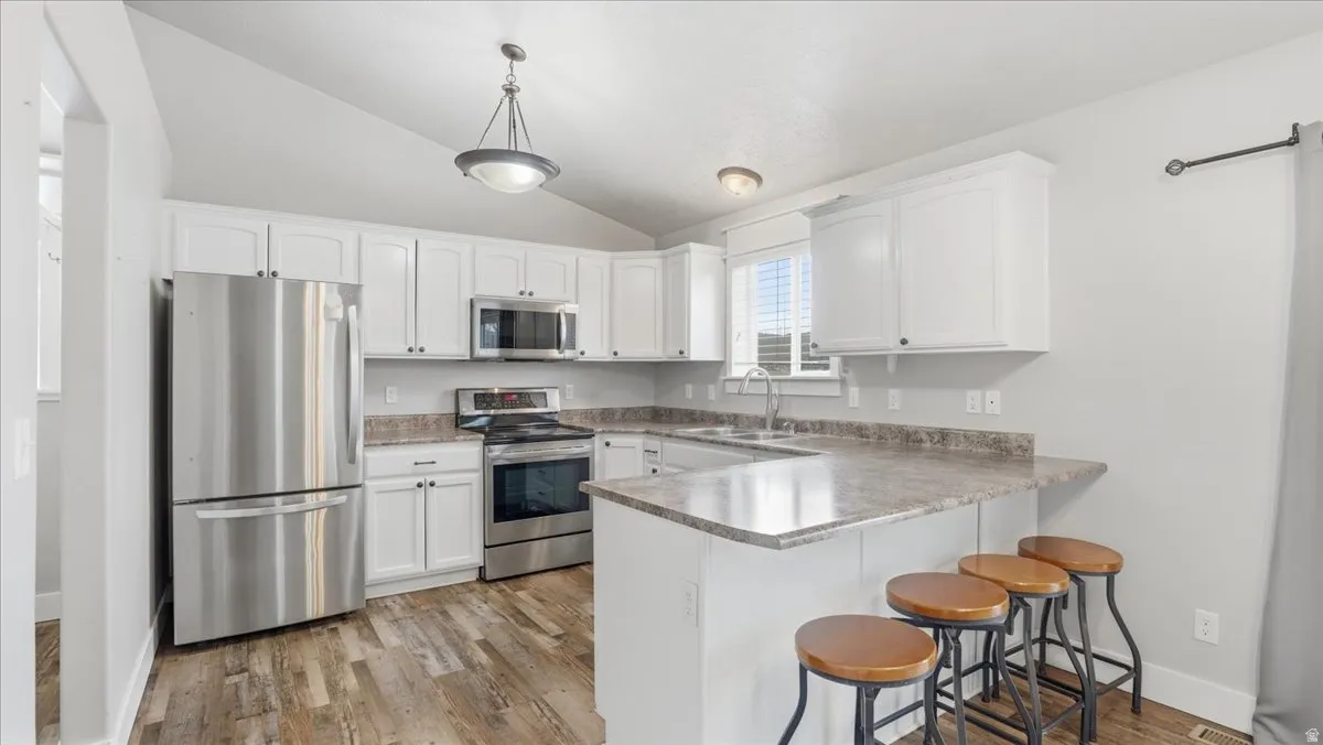 Kitchen with stainless steel appliances, a peninsula, a breakfast bar area, white cabinets, and vaulted ceiling