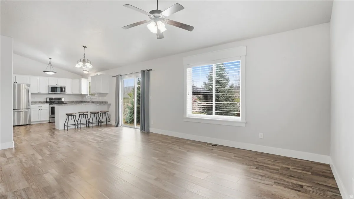 Unfurnished living room with lofted ceiling, light wood-type flooring, hanging lights, and ceiling fan