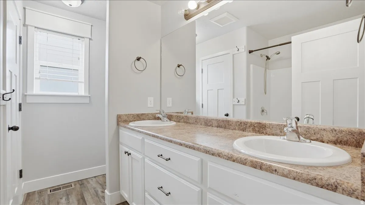 Primary bedroom full bath featuring double vanity, light wood finished floors, and a shower