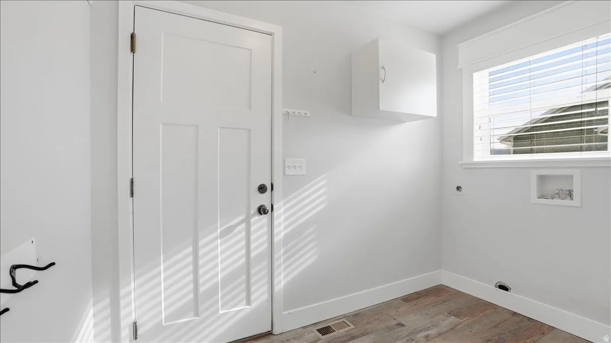 Laundry room with hookup for an electric dryer, light wood-type flooring, and washer hookup.  Entrance to garage.