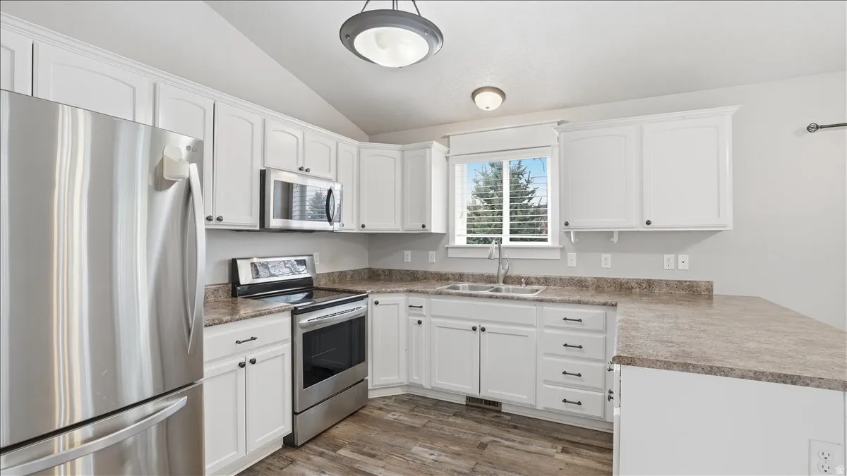 Kitchen with stainless steel appliances, white cabinetry, vaulted ceiling, a peninsula, and dark wood-type flooring