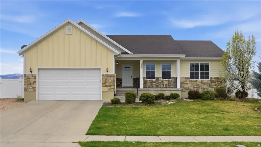 View of front facade featuring stone siding, covered porch, board and batten siding, a garage, and driveway