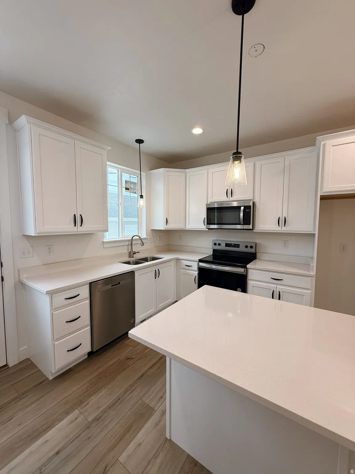 Kitchen with white cabinets, stainless steel appliances, decorative light fixtures, and light wood-style flooringPhotos are for reference only.  Actual finishes may vary.