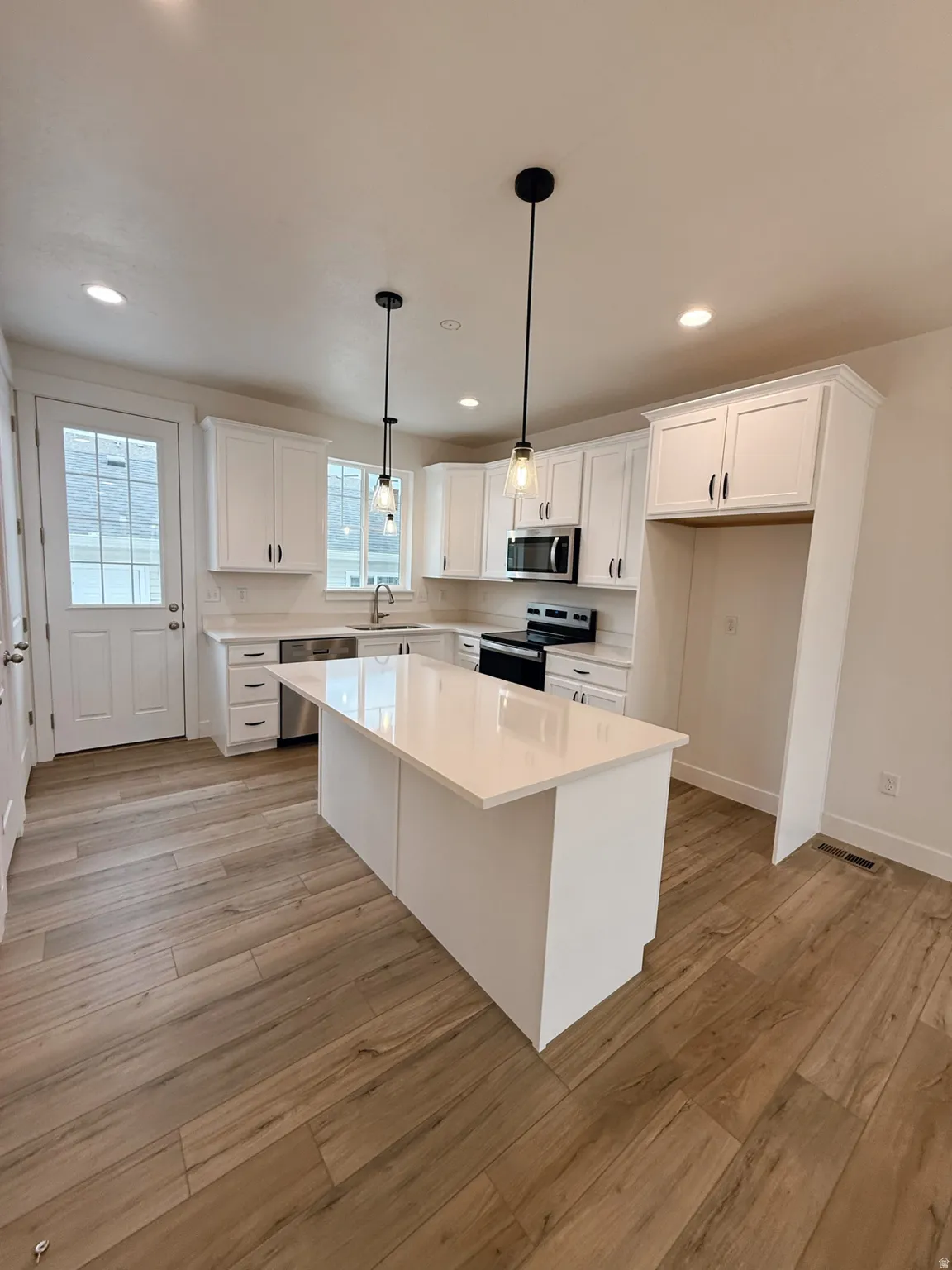 Kitchen with stainless steel appliances, white cabinets, light wood finished floors, and a center islandPhotos are for reference only.  Actual finishes may vary.