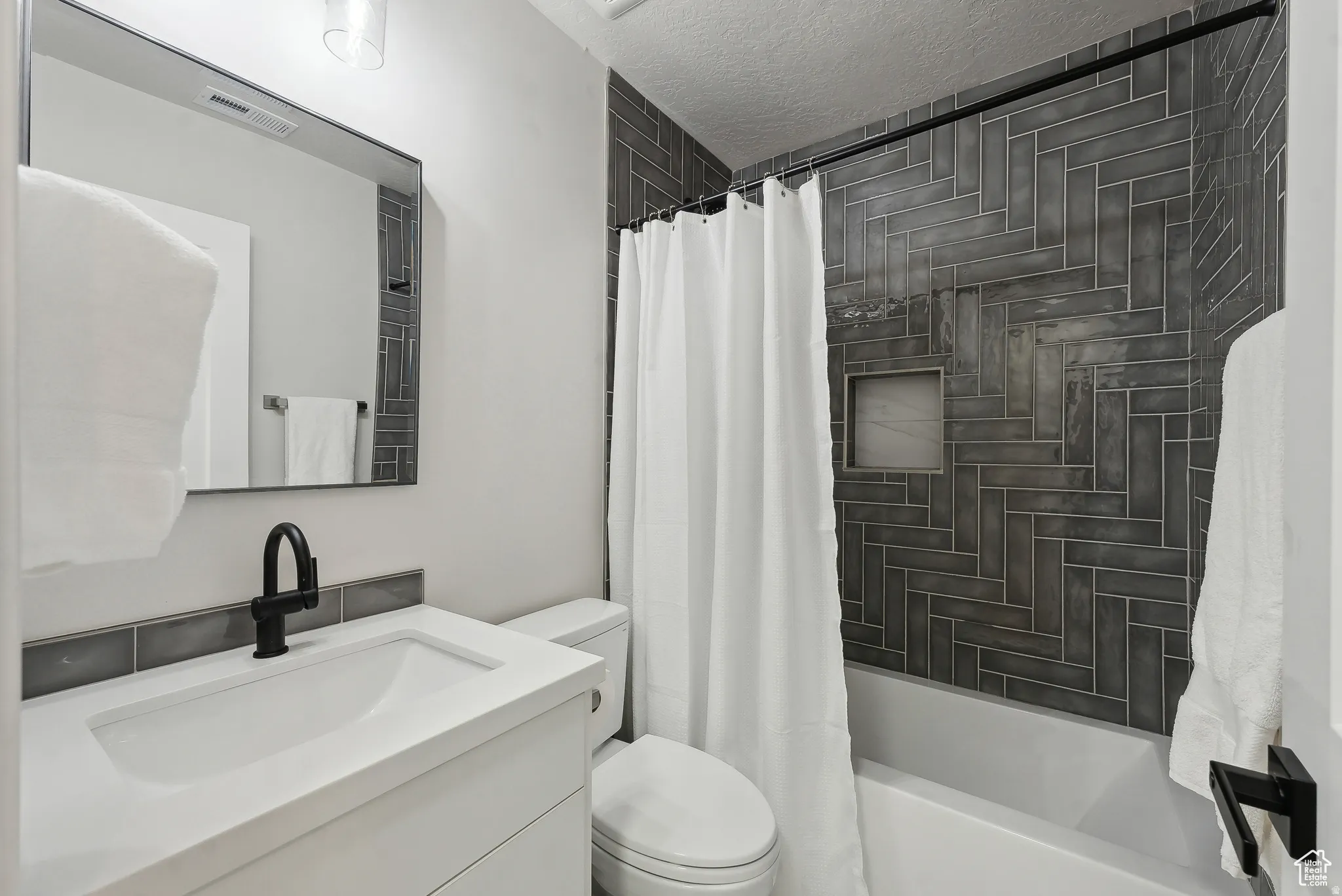 Full bath with vanity, shower / tub combo, and a textured ceiling