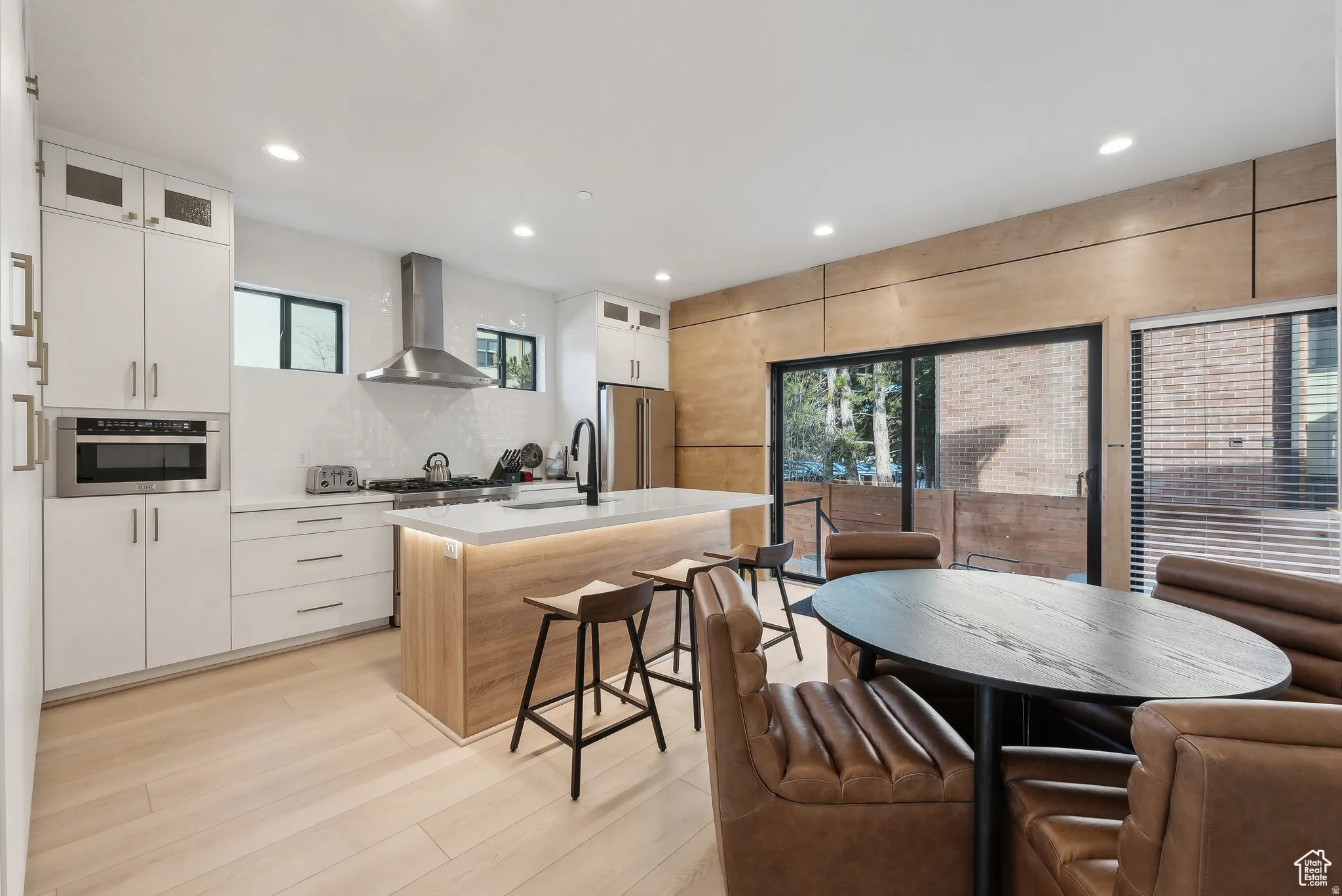 Dual tone kitchen with glass insert cabinets, a kitchen island with sink, light wood-style floors, high quality fridge, and two tone cabinets