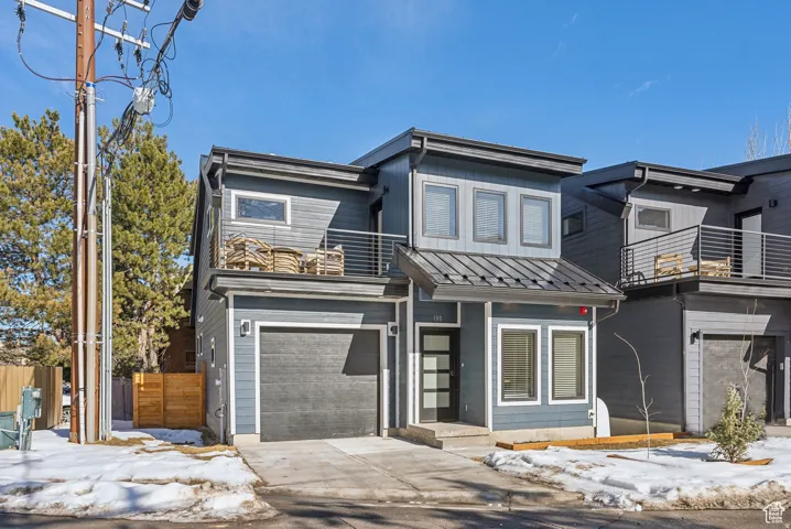 Contemporary home featuring an attached garage, a standing seam roof, driveway, and a balcony