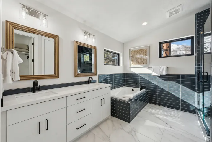 Full bath featuring vaulted ceiling, double vanity, a bath, a stall shower, and recessed lighting