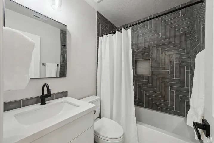 Full bath with vanity, shower / tub combo, and a textured ceiling