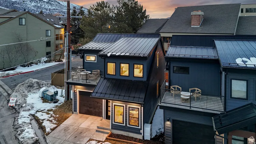 View of front of property with a standing seam roof, an attached garage, concrete driveway, a chimney, and a balcony