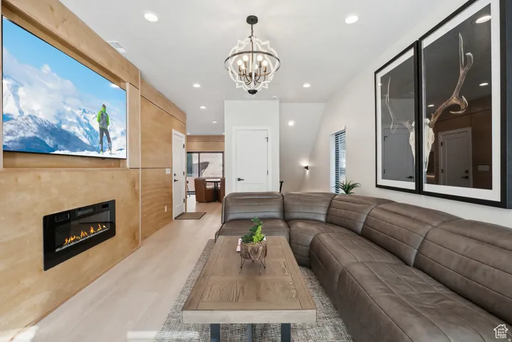 Living room featuring light wood-style flooring, a glass covered fireplace, and hanging lights