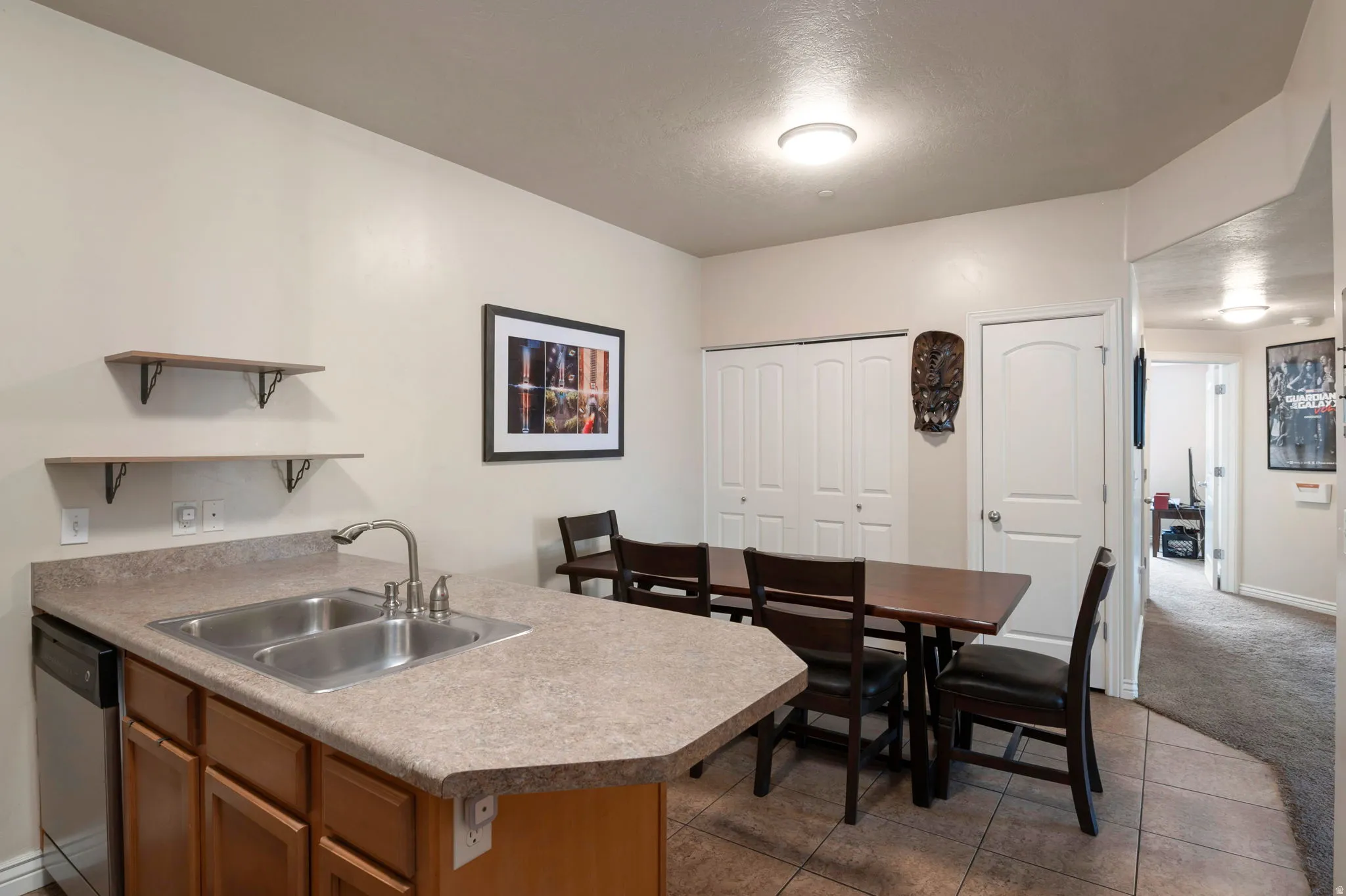 Kitchen featuring a peninsula, open shelves, stainless steel dishwasher, light countertops, and wood finish cabinetry