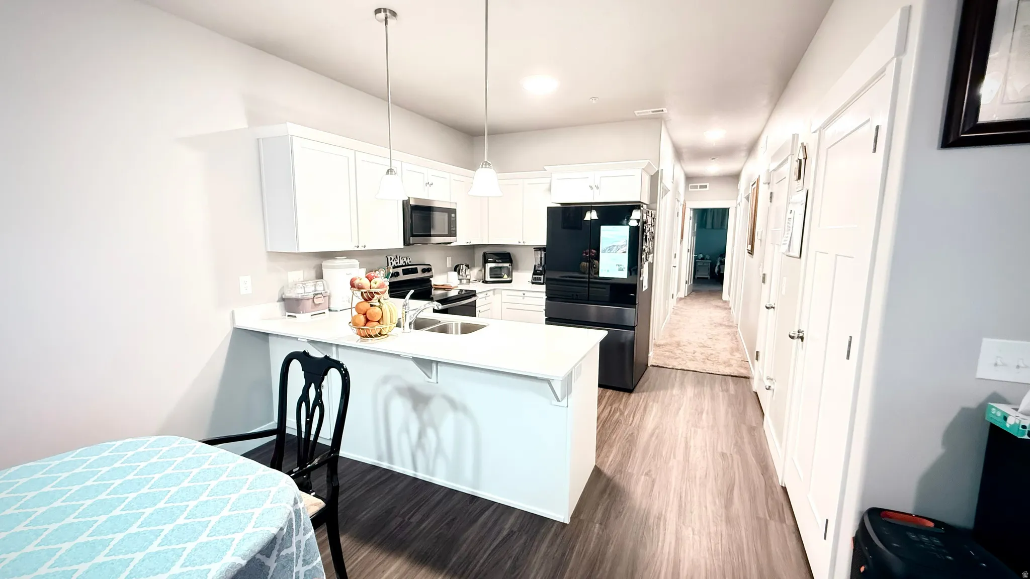 Kitchen featuring stainless steel appliances, a peninsula, white cabinets, a breakfast bar, and dark wood-style floors