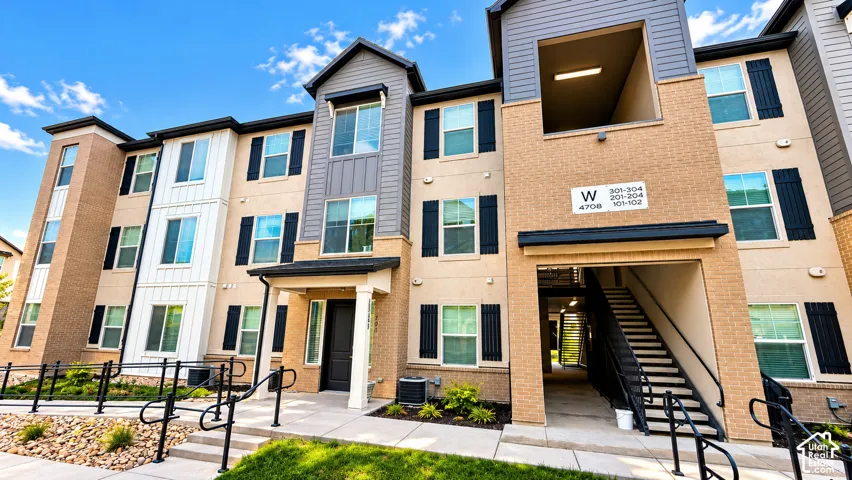 Multi-story building exterior featuring a combination of brick and siding, multiple windows with black shutters, and an integrated exterior stairway