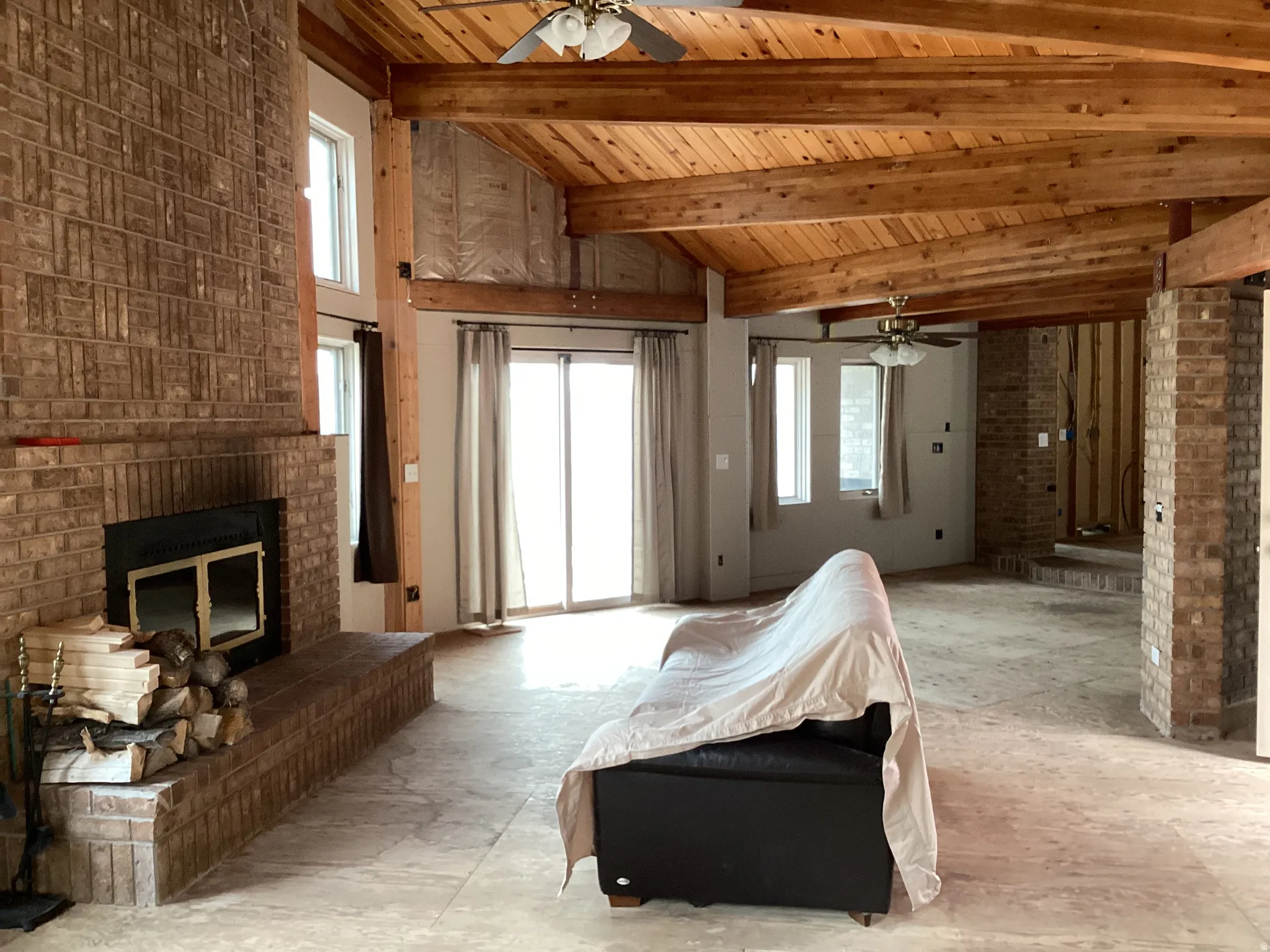 Living area with a ceiling fan, a fireplace, healthy amount of natural light, brick wall, and a high wooden beamed ceiling