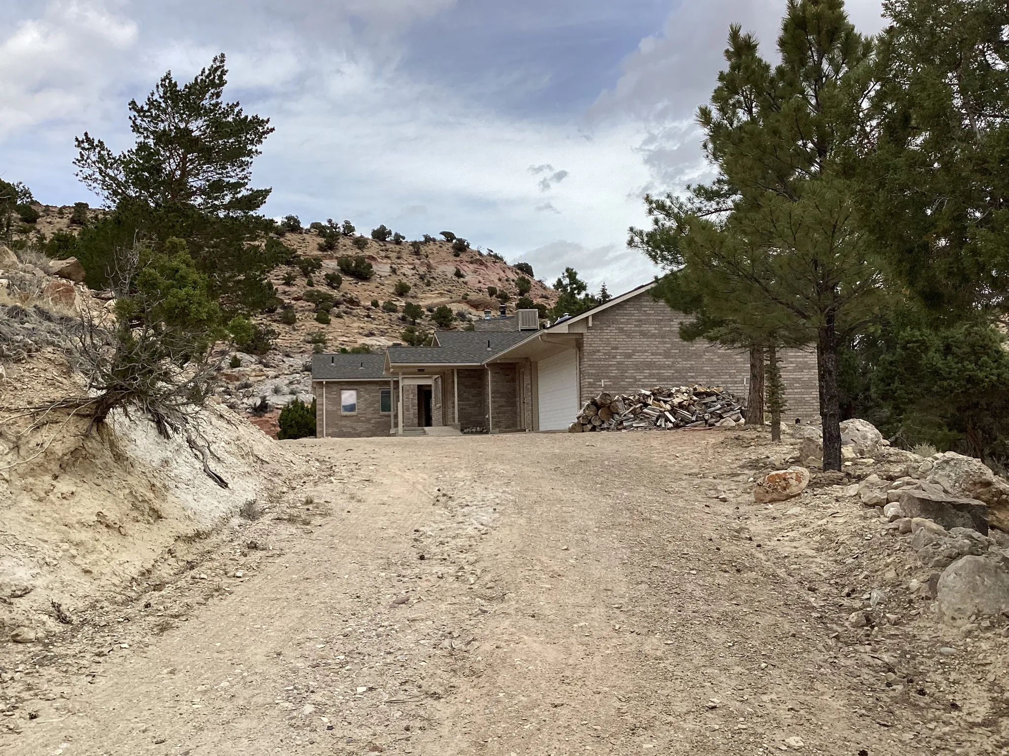 View of front of house featuring a patio area, brick siding, an attached garage, and dirt driveway