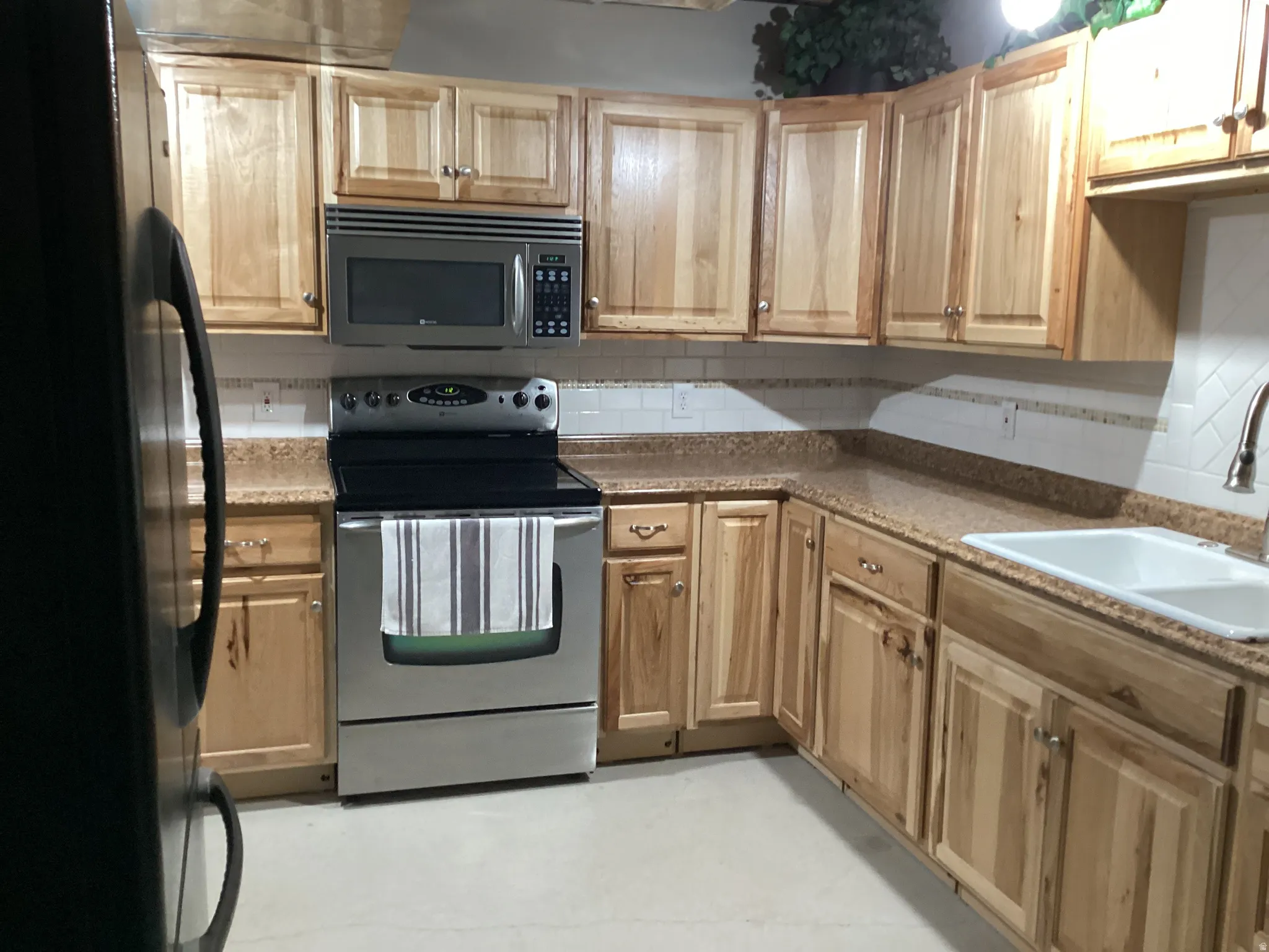 Kitchen featuring stainless steel appliances, tasteful backsplash, light wood finish cabinets, and dark stone countertops